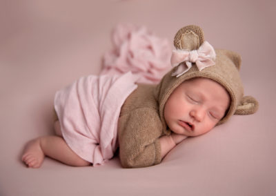 newborn baby on pink background in bear suit