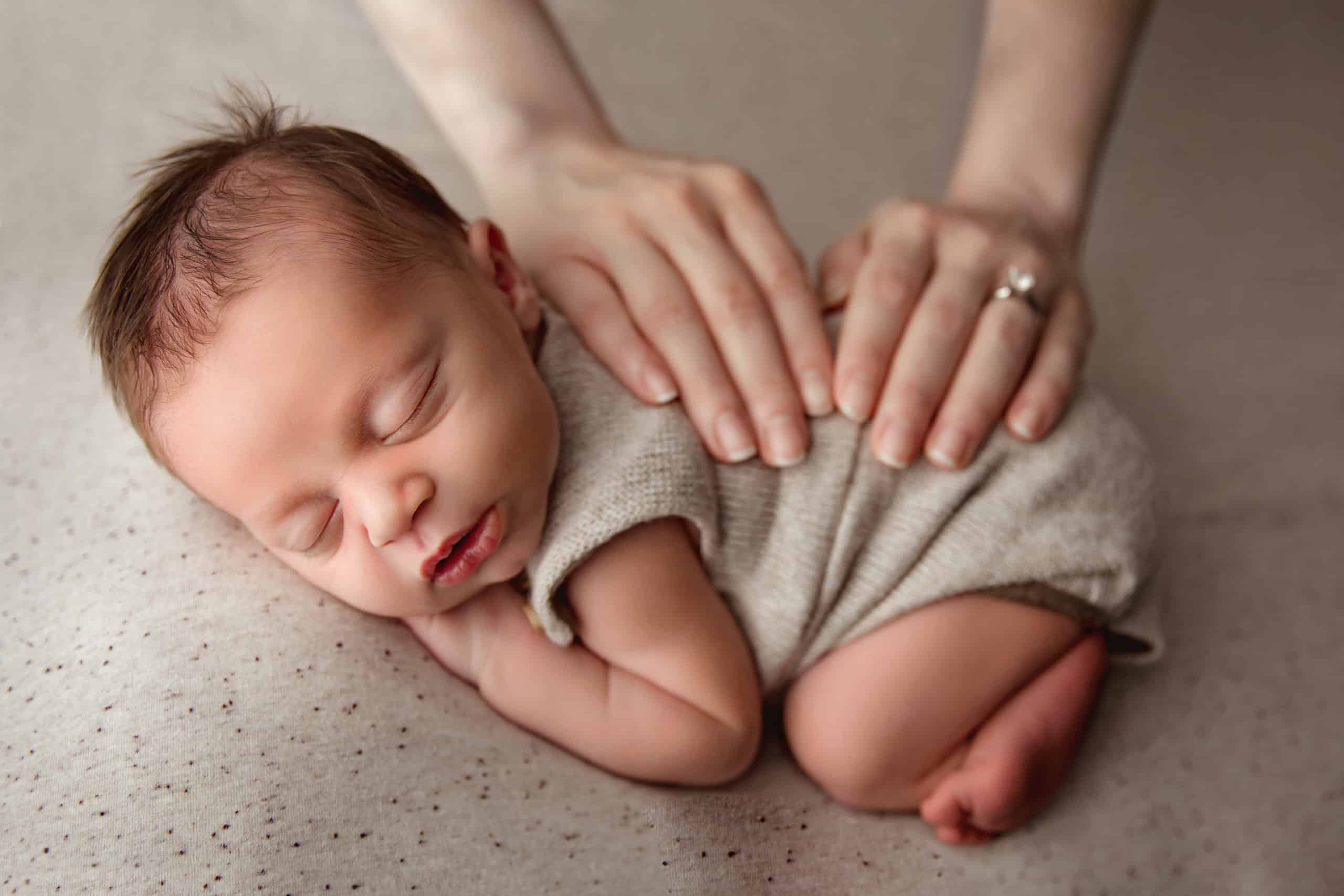 newborn baby with moms hands on him